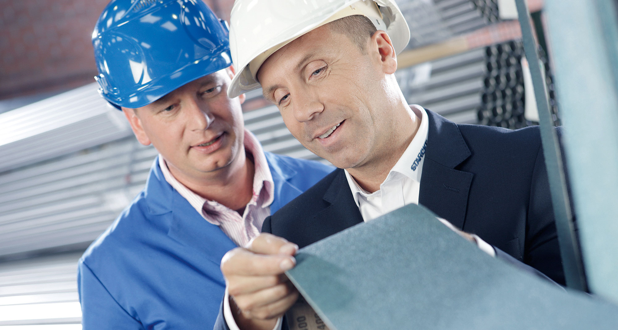 Zwei Männer prüfen ein Metallblech. Beide tragen einen Helm.